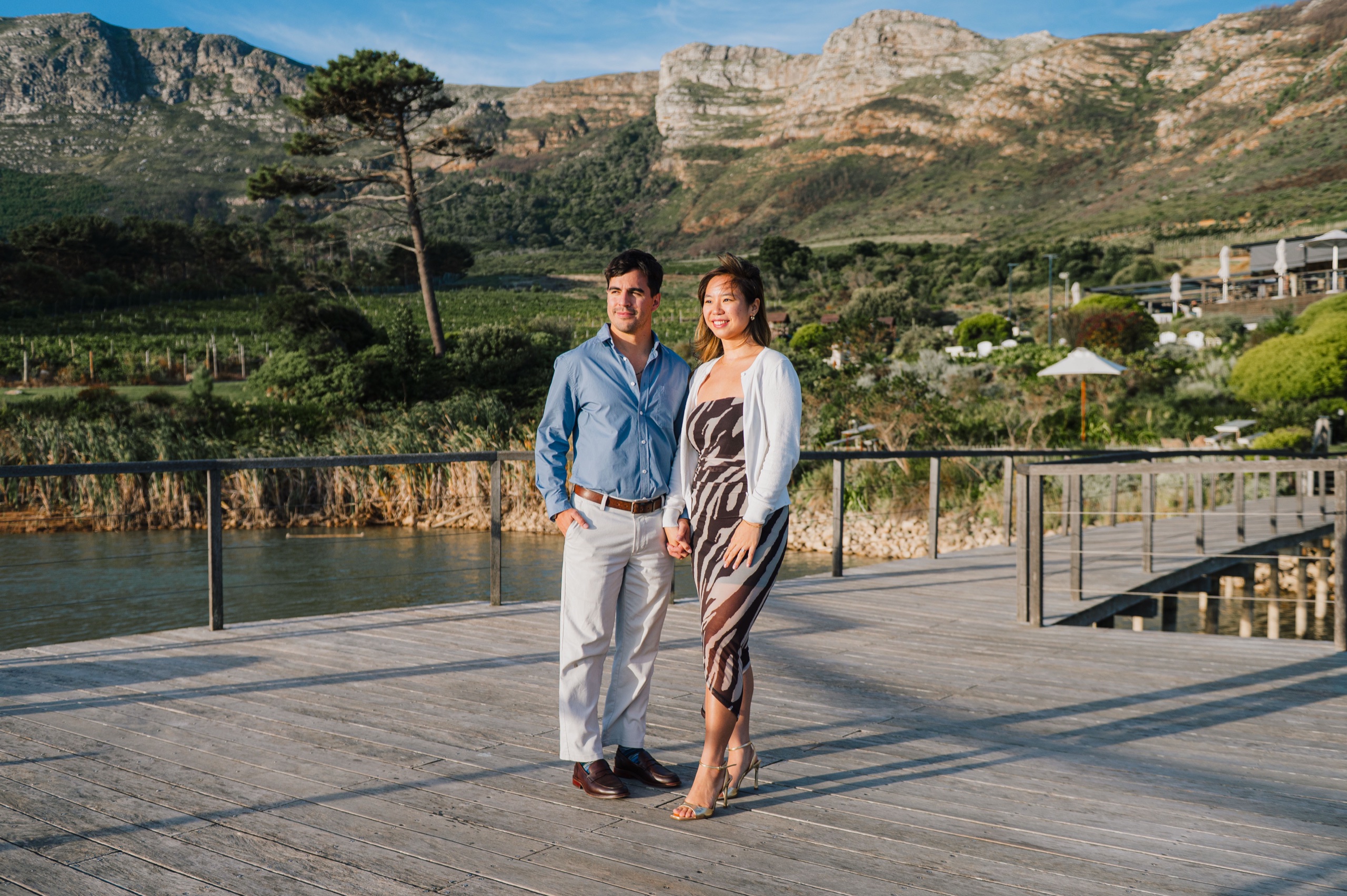 Cris and Vanessa standing hand in hand on a deck beneath the mountains